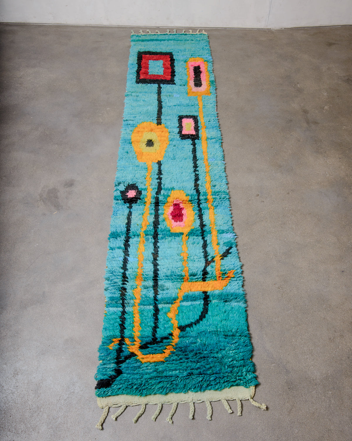Vintage Berber runner rug made of colourful wool, laying on concrete floor.
